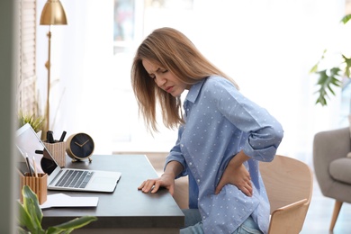 Photo of Young woman suffering from back pain in office