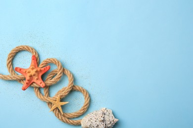 Beautiful starfishes, sea shell, rope and sand on light blue background, flat lay. Space for text