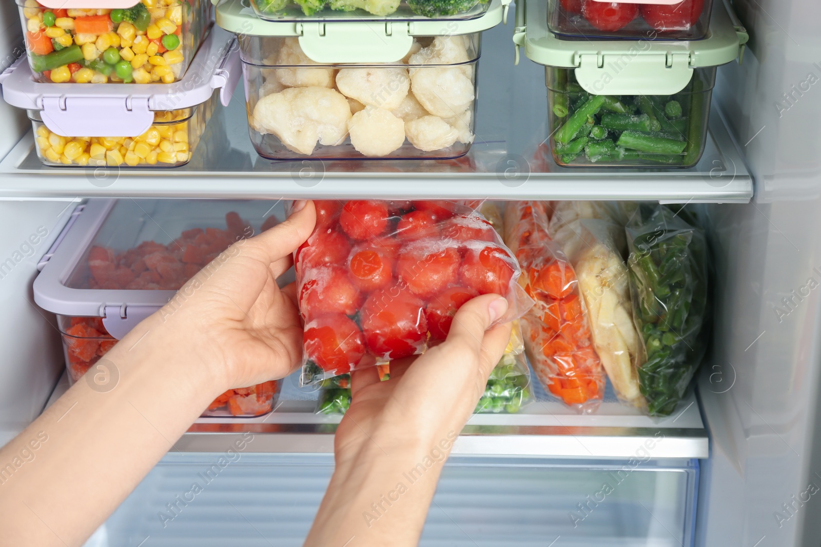 Photo of Woman taking plastic bag with frozen tomatoes from refrigerator, closeup