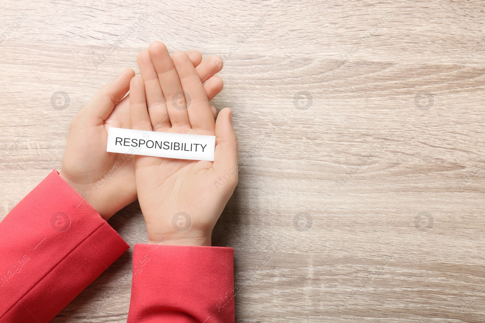 Photo of Woman holding card with word Responsibility at wooden table, top view