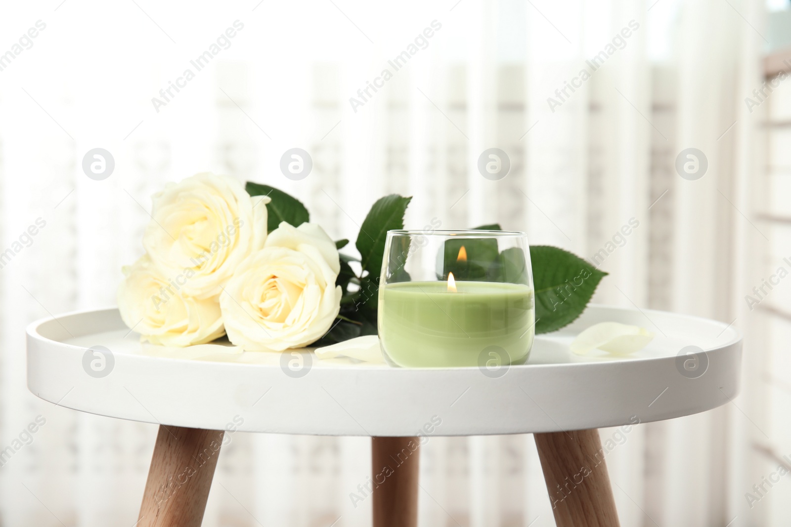 Photo of Burning candle in glass holder and roses on white table