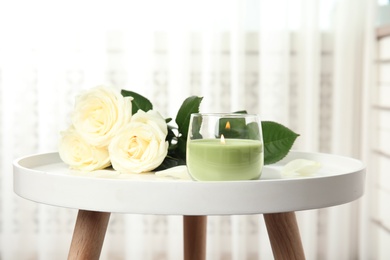 Burning candle in glass holder and roses on white table