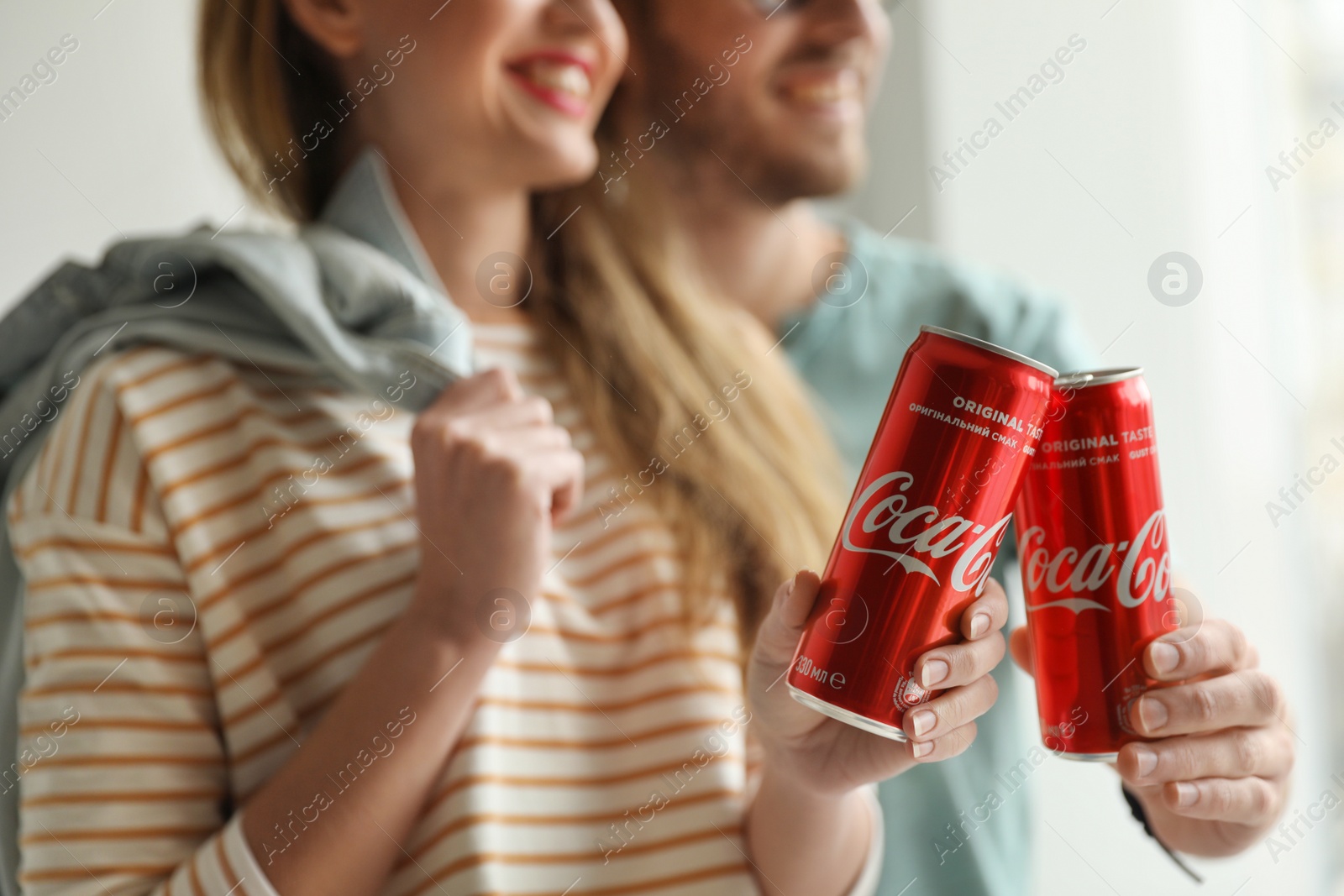 Photo of MYKOLAIV, UKRAINE - NOVEMBER 28, 2018: Young couple with Coca-Cola cans indoors, closeup