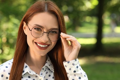Photo of Portrait of happy young woman with glasses outdoors. Space for text. Lady with beautiful smile looking into camera