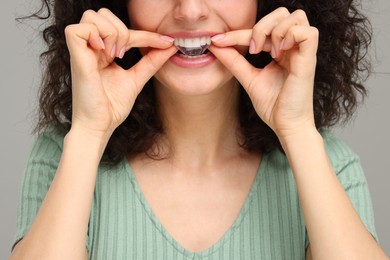 Young woman applying whitening strip on her teeth against grey background, closeup