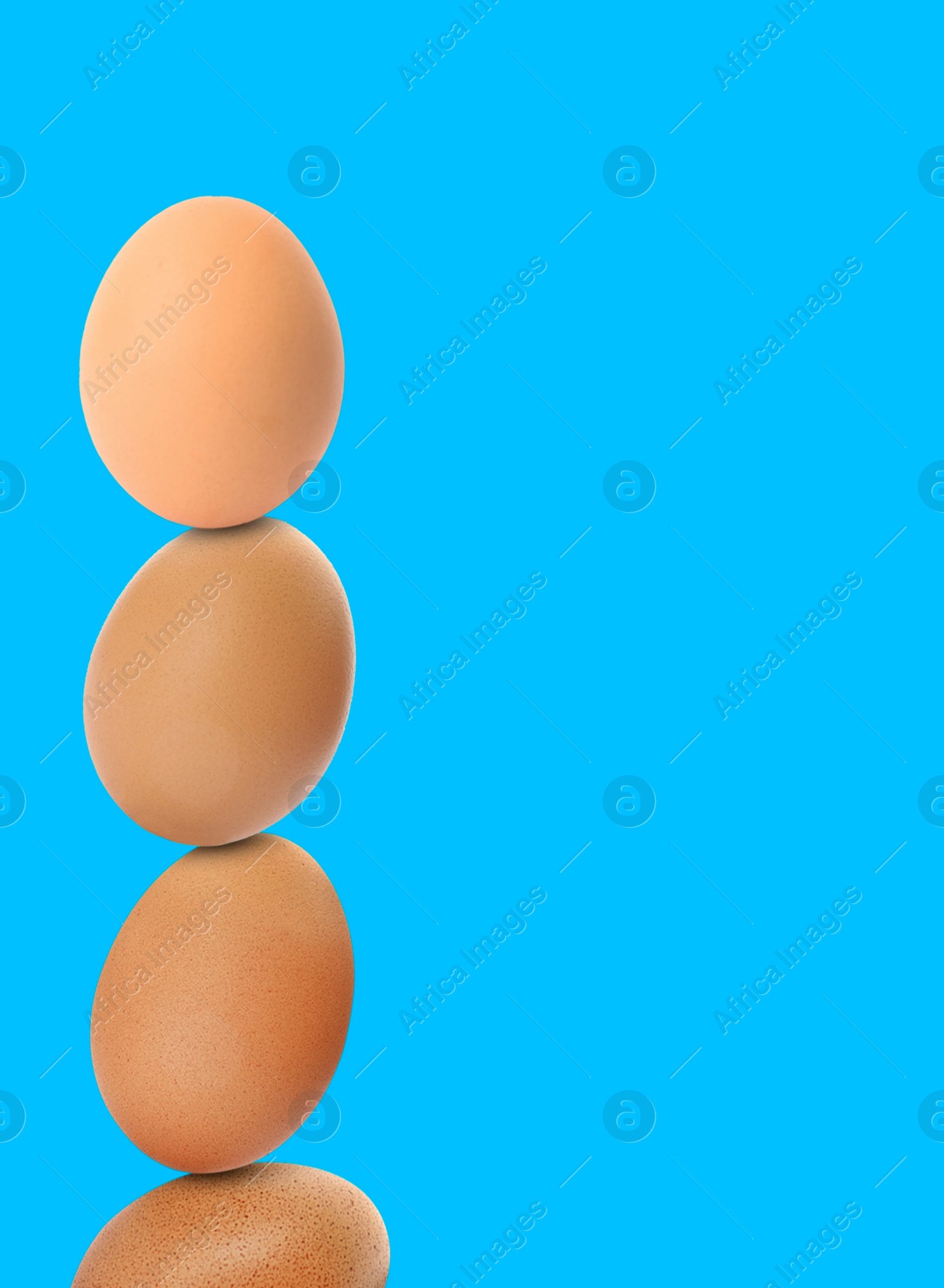 Image of Stacked fresh chicken eggs against light blue background. Space for text