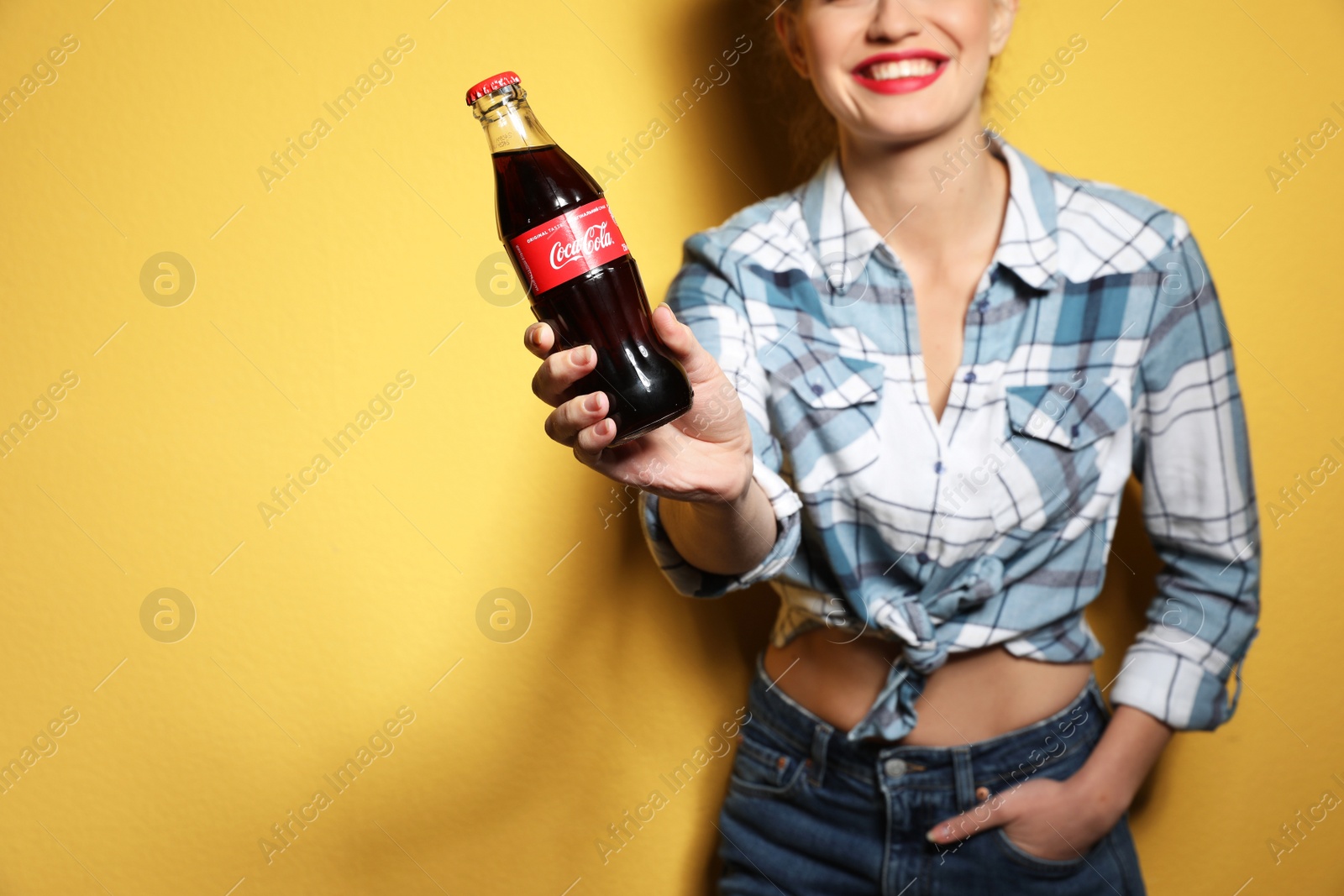 Photo of MYKOLAIV, UKRAINE - NOVEMBER 28, 2018: Young woman with bottle of Coca-Cola on color background, space for text