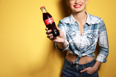 Photo of MYKOLAIV, UKRAINE - NOVEMBER 28, 2018: Young woman with bottle of Coca-Cola on color background, space for text