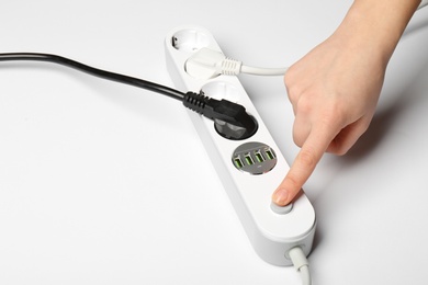 Woman pressing power button of extension cord on white background, closeup. Electrician's equipment