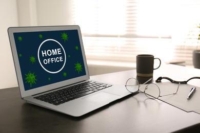 Image of Modern laptop with text HOME OFFICE on table indoors