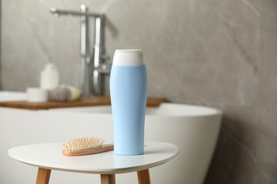 Bottle of shampoo and wooden hairbrush on white table in bathroom, space for text