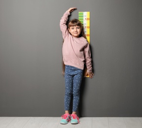 Photo of Little girl measuring her height near grey wall