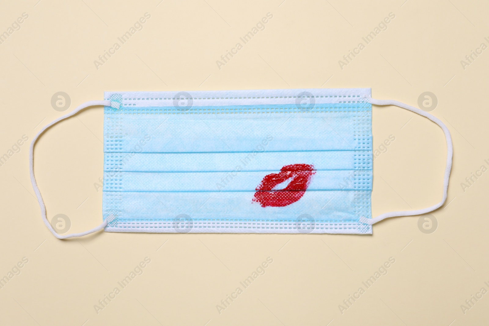Photo of Medical mask with lipstick mark on beige background, top view