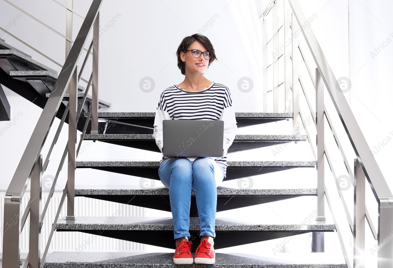 Photo of Young woman with modern laptop sitting on stairs indoors