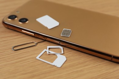 Photo of SIM cards, mobile phone and ejector tool on wooden table