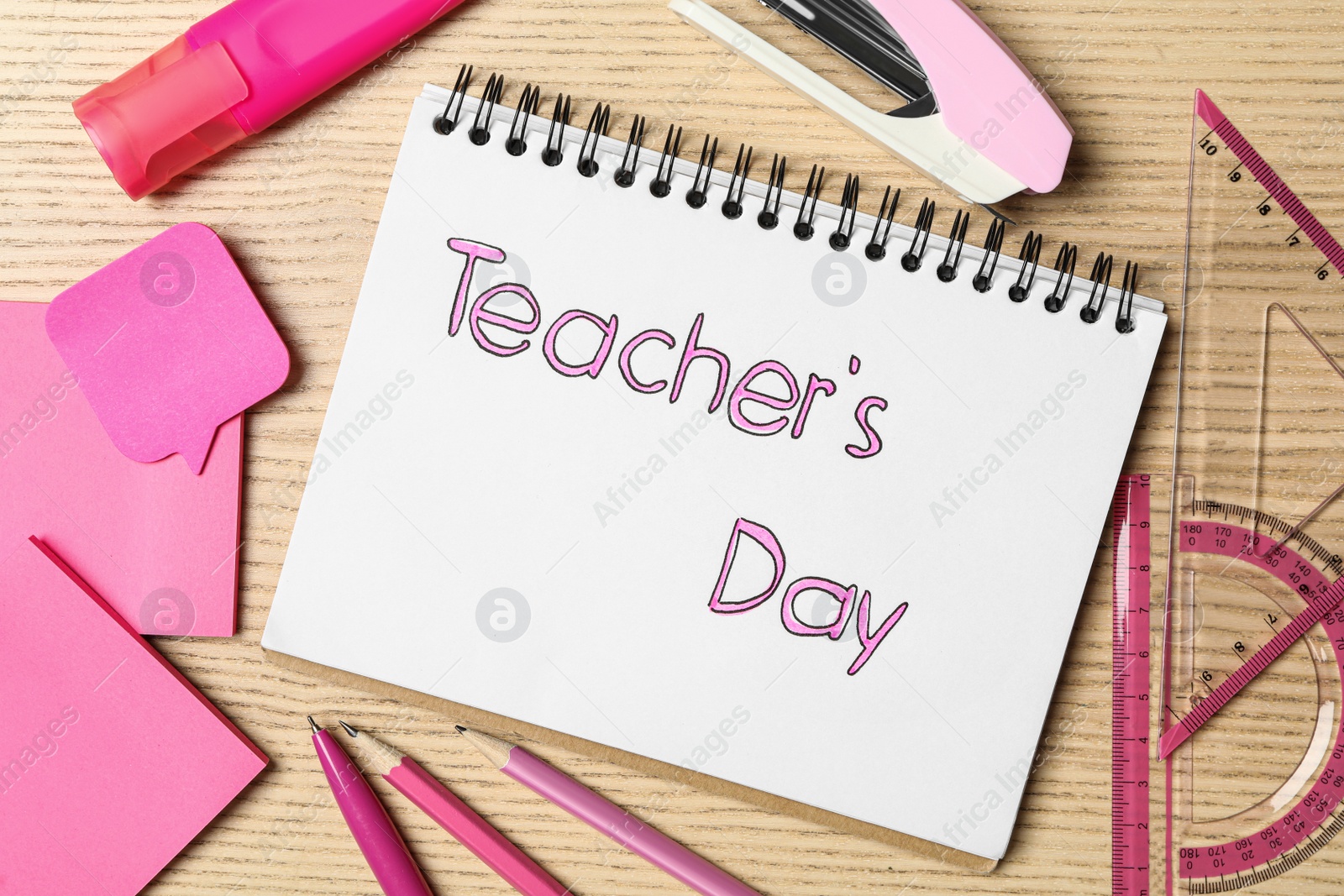 Photo of Notebook with words TEACHER'S DAY and set of pink stationery on wooden table, flat lay