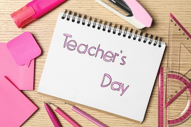 Notebook with words TEACHER'S DAY and set of pink stationery on wooden table, flat lay