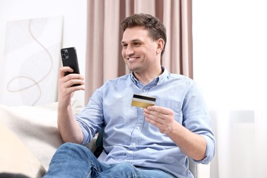 Photo of Happy man with credit card and smartphone shopping online at home