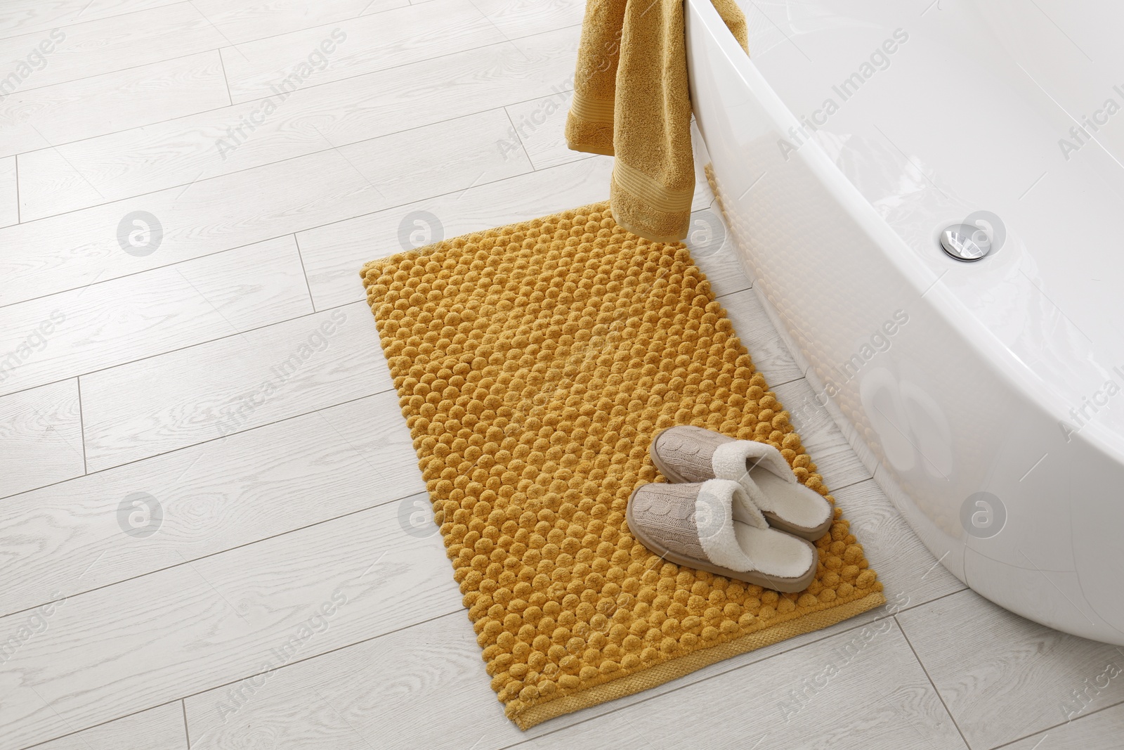 Photo of Soft orange bath mat and slippers on floor in bathroom