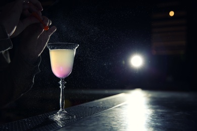 Photo of Barman adding lemon zest into cosmopolitan martini cocktail at counter, closeup. Space for text