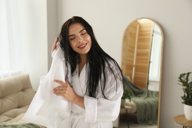 Photo of Beautiful young woman in bathrobe drying hair with towel indoors