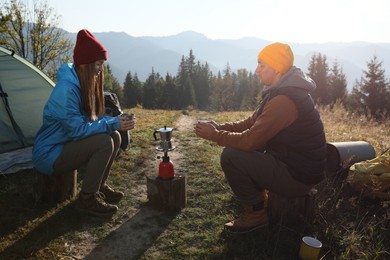 Young couple drinking coffee near camping tents in mountains