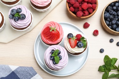 Sweet cupcakes with fresh berries on light wooden table, flat lay