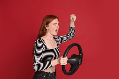 Photo of Emotional young woman with steering wheel on red background