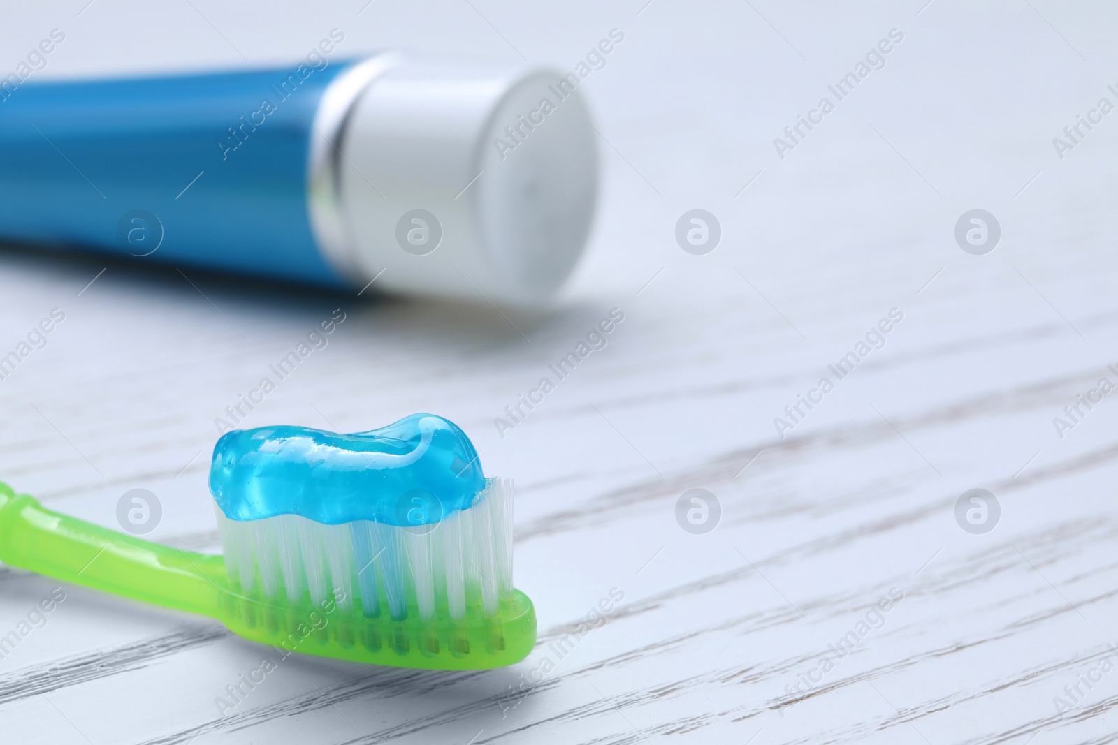 Photo of Brush with toothpaste and tube on white wooden table, closeup. Space for text