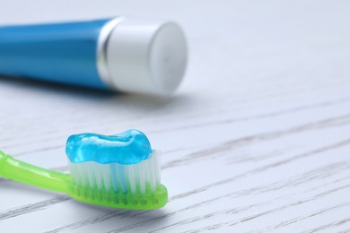 Brush with toothpaste and tube on white wooden table, closeup. Space for text