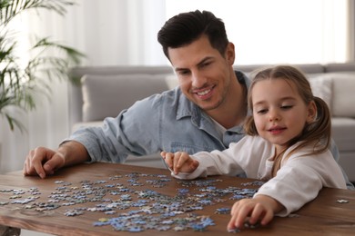 Photo of Man and his little daughter playing with puzzles at home