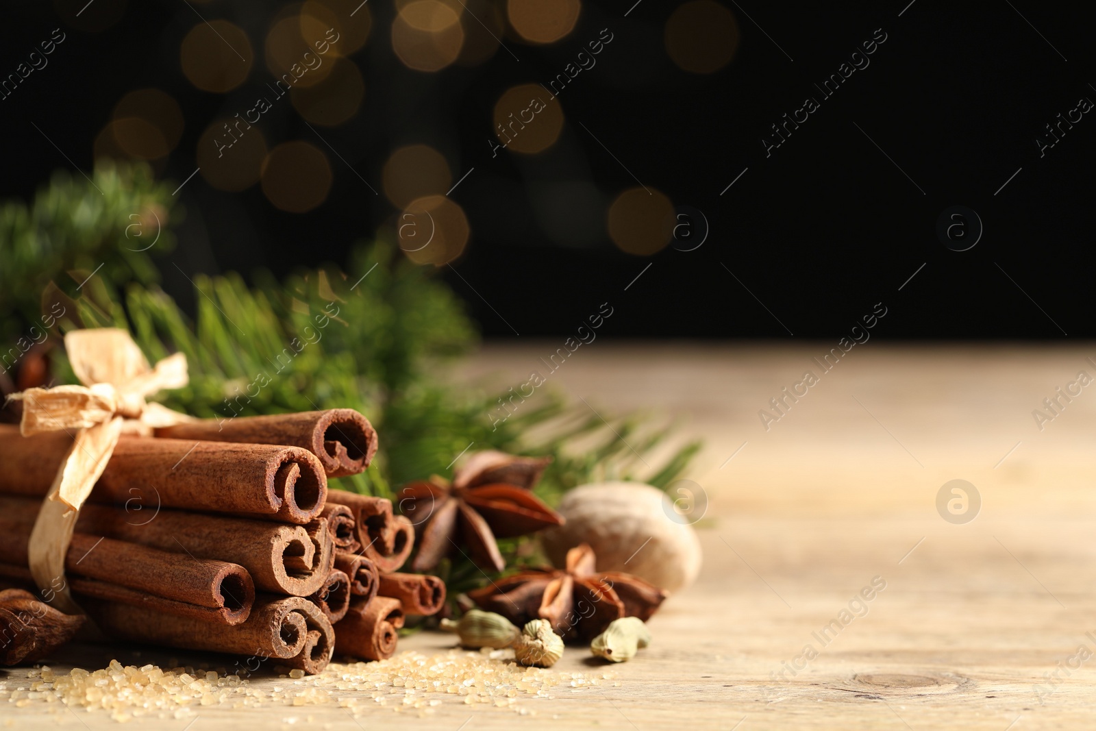 Photo of Different aromatic spices on wooden table against black background, closeup. Space for text