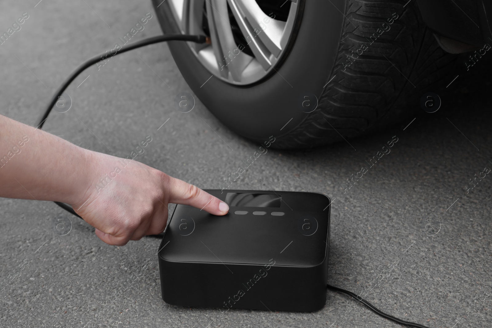 Photo of Man using portable air pump to inflate car tire outdoors, closeup