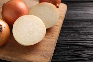 Photo of Whole and cut ripe onions on black wooden table, closeup. Space for text