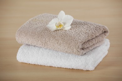 Photo of Soft folded towels with orchid flower on wooden table