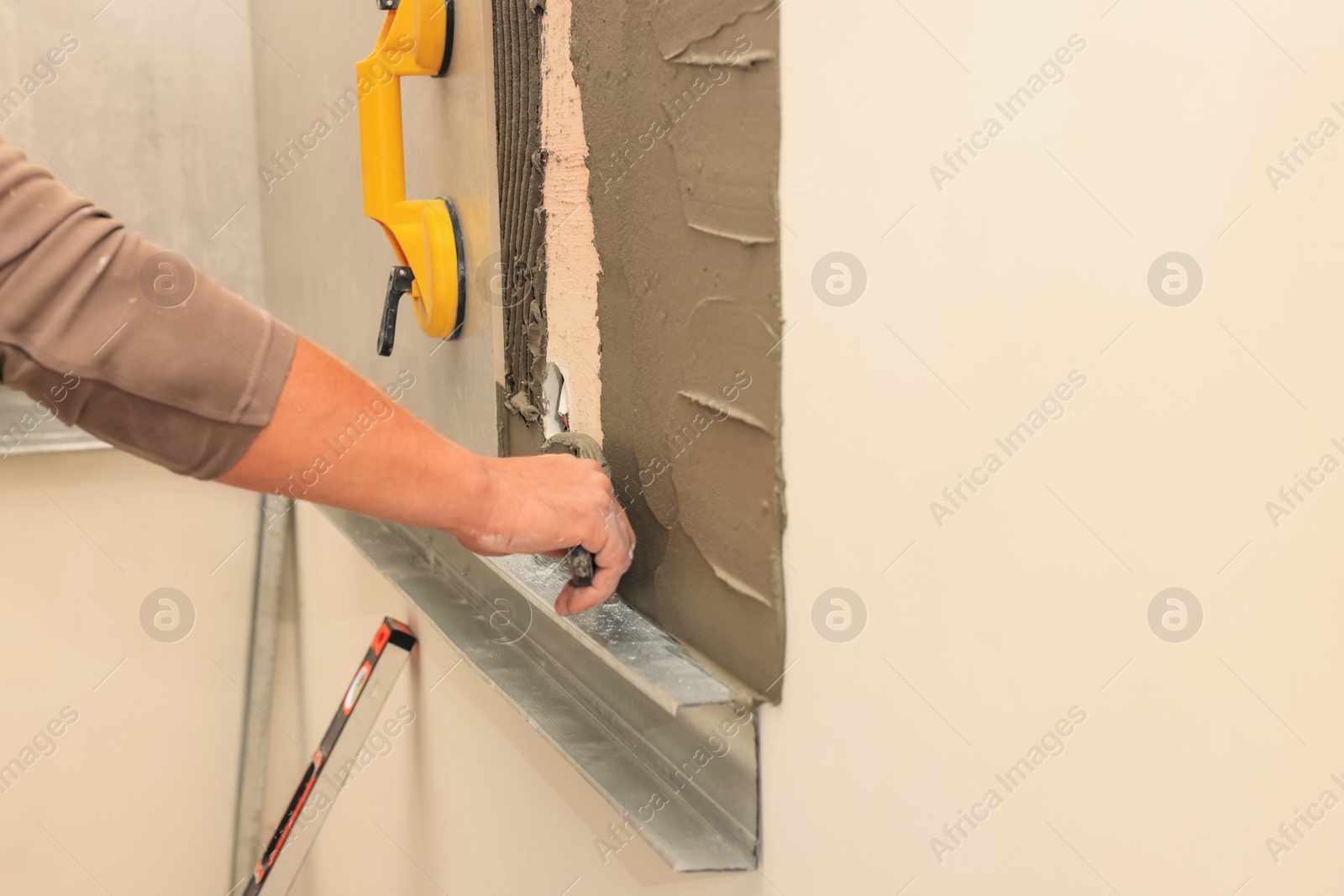 Photo of Worker spreading adhesive mix on wall for tile installation indoors, closeup