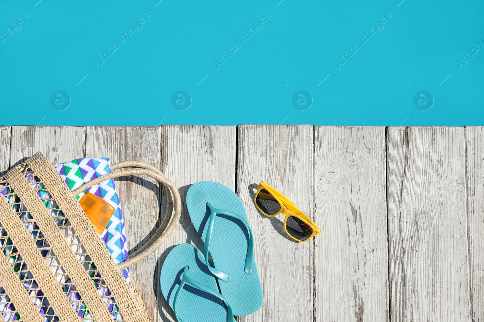 Photo of Beach accessories on wooden deck near outdoor swimming pool, flat lay. Space for text