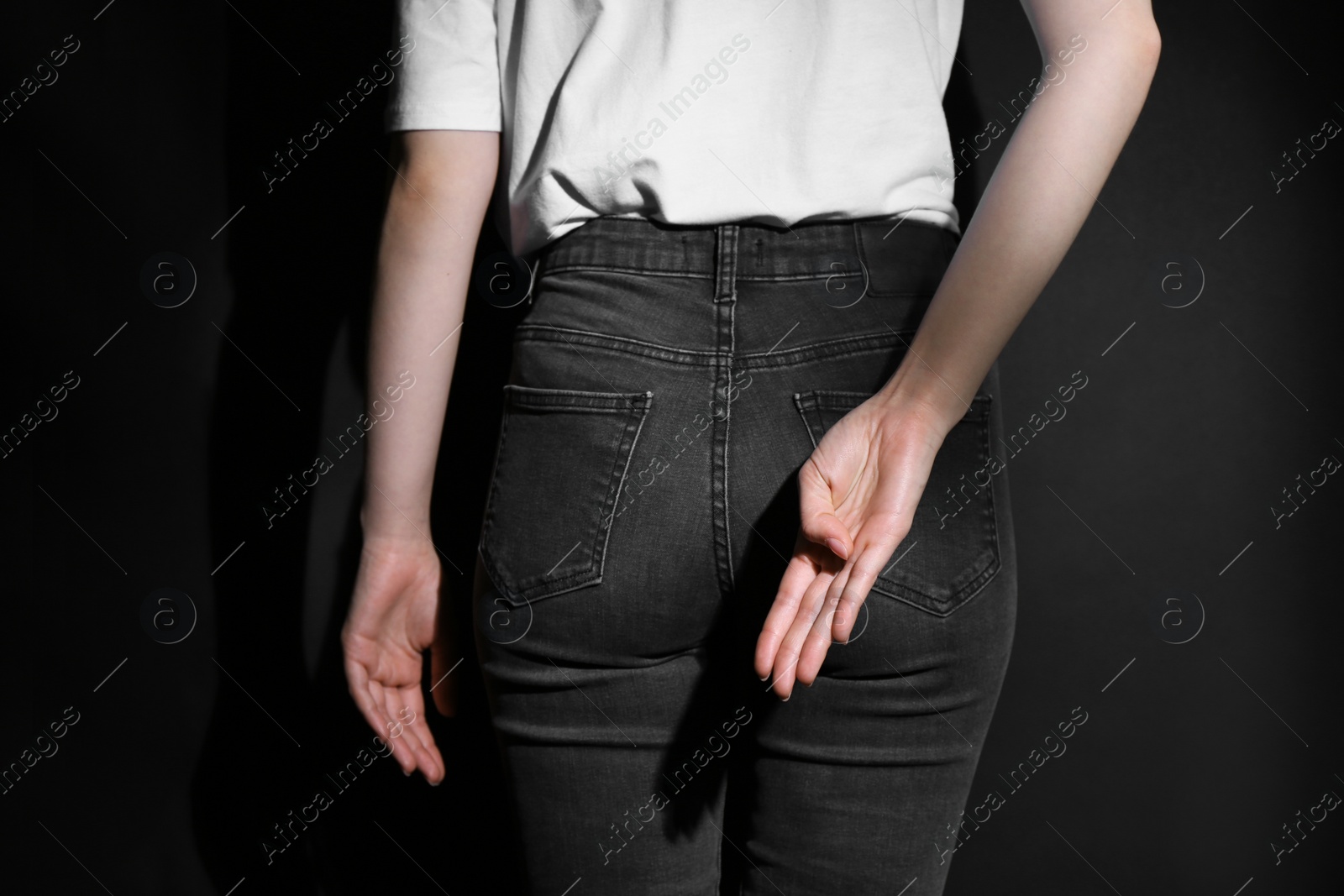 Photo of Woman showing open palm behind her back on black background, back view