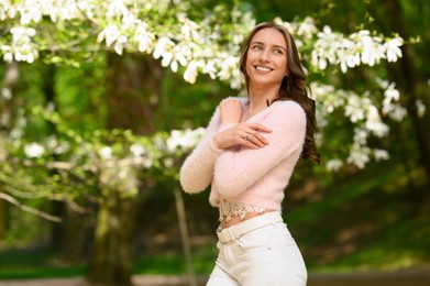 Beautiful young woman near blossoming tree on spring day, space for text