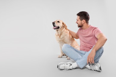 Photo of Man with adorable Labrador Retriever dog on light gray background, space for text. Lovely pet