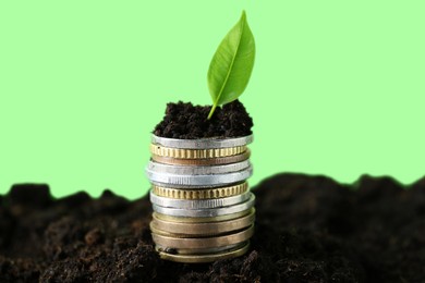 Photo of Stack of coins and green plant on soil against blurred background, closeup. Profit concept