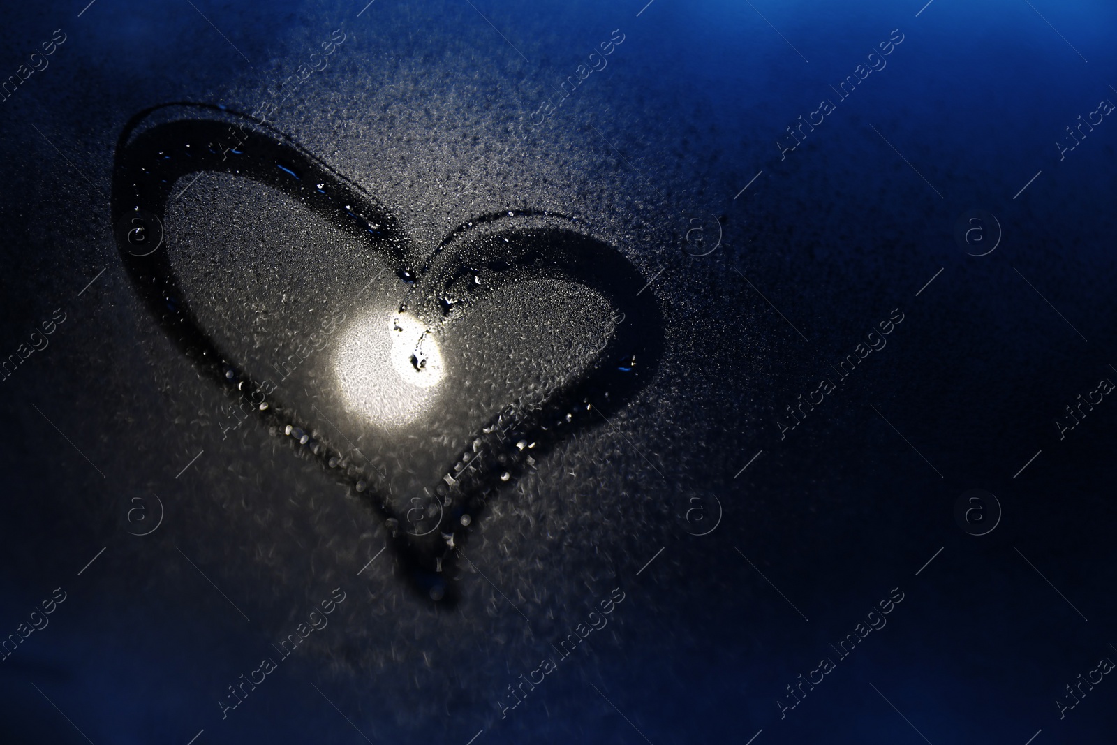 Photo of Glass with heart drawn in condensation against dark background. Space for text