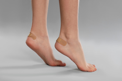 Photo of Girl showing feet with sticking plasters on light grey background, closeup