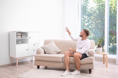 Photo of Young man with air conditioner remote at home