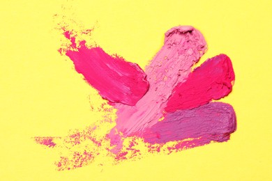 Smears of different beautiful lipsticks on yellow background, top view