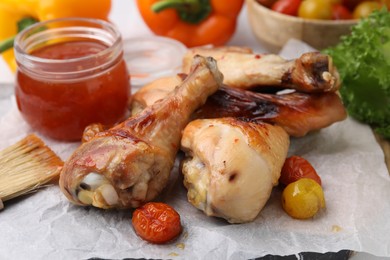 Photo of Marinade, basting brush, roasted chicken drumsticks and tomatoes on table, closeup