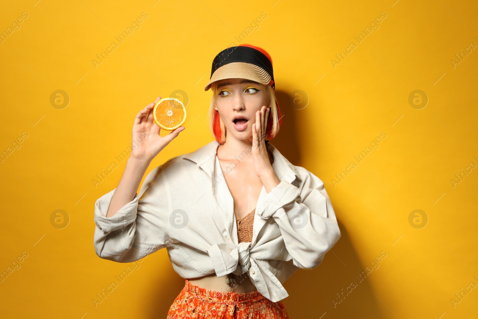 Photo of Emotional young woman with bright dyed hair holding orange half on color background