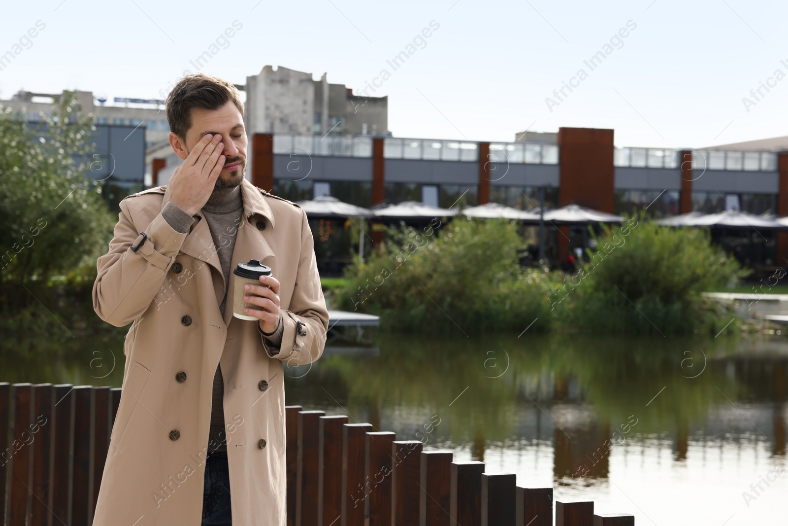 Photo of Sleepy man with cup of coffee near river outdoors. Space for text