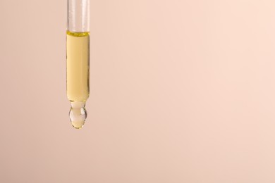 Photo of Dripping cosmetic serum from pipette on beige background, space for text