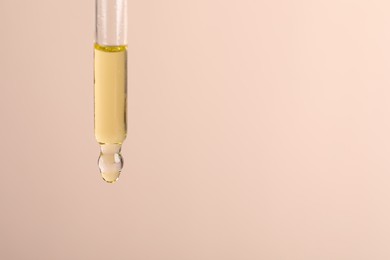 Dripping cosmetic serum from pipette on beige background, space for text